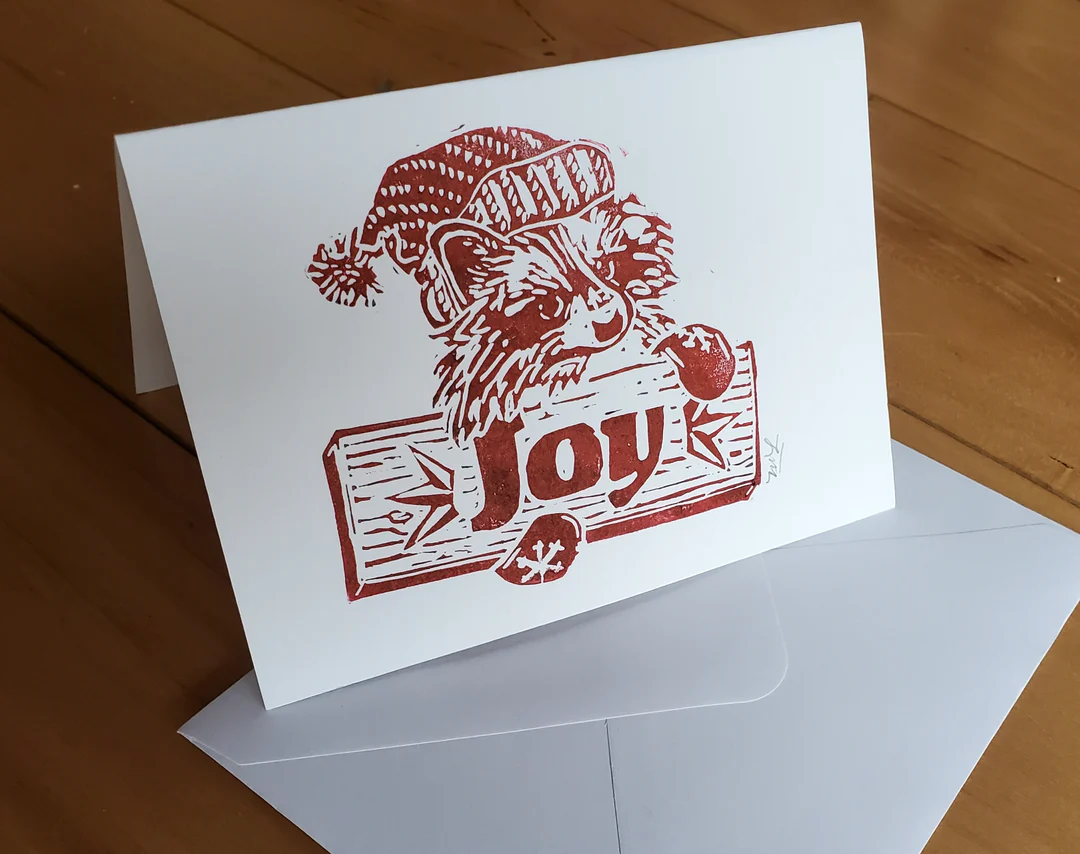 holiday card with  racoon holding sign that says Joy